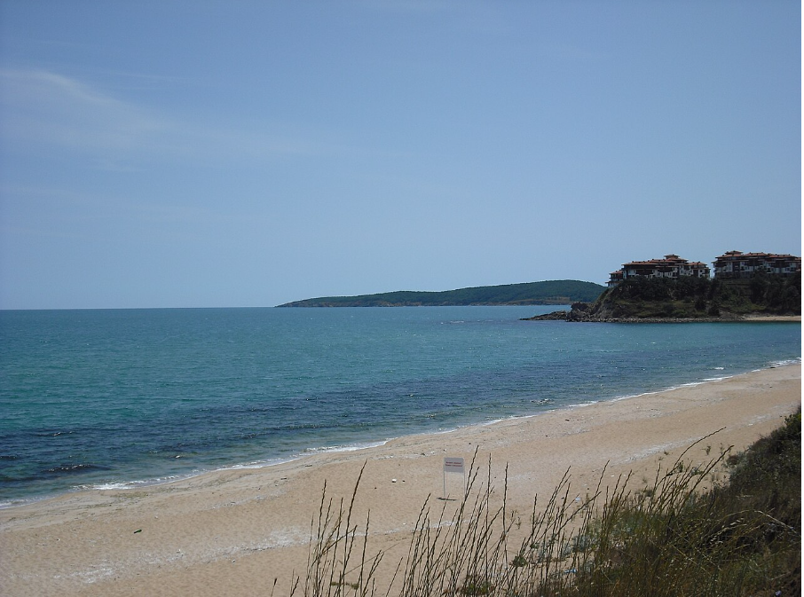 Спокойно море, див плаж и част от жилищен комплекс в далечината.
